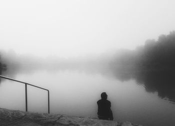 Rear view of teenage boy looking at lake against sky during foggy weather