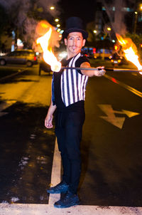 Full length portrait of man performing with fire on street at night