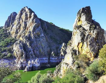 Rock formation by mountains against clear sky