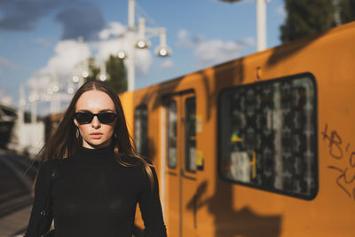 Portrait of young woman wearing sunglasses while standing against train