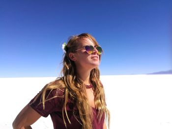 Beautiful young woman standing salar de uyuni against clear blue sky