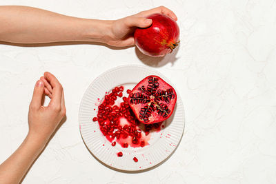 The woman's hands are holding a ripe pomegranate on a white table.