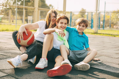 Cheerful high school students sit on the basketball court, relax after the game, talk and laugh. 