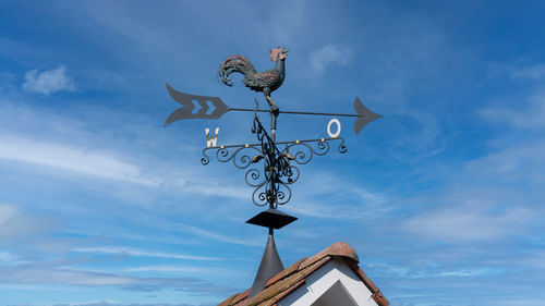 Low angle view of weather vane against cloudy sky