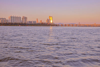 Scenic view of sea by buildings against sky during sunset