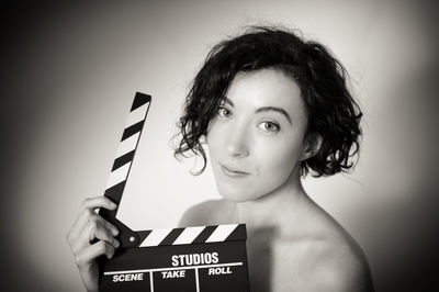 Portrait of beautiful naked woman holding film slate against wall