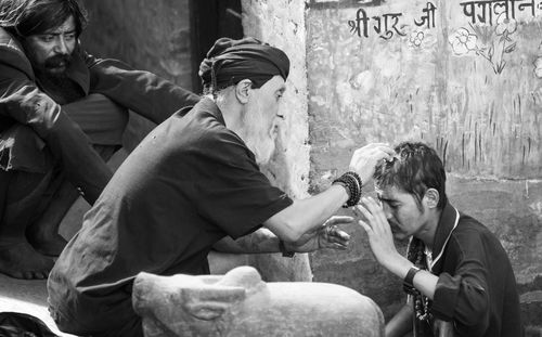 Portrait of young man holding woman sitting against wall