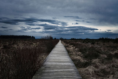 Empty boardwalk leading towards landscape against sky