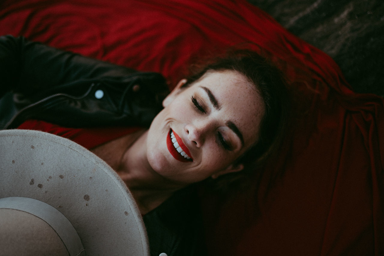 young adult, smiling, lying down, one person, portrait, emotion, lifestyles, leisure activity, real people, young women, relaxation, headshot, happiness, eyes closed, high angle view, women, indoors, casual clothing, beautiful woman