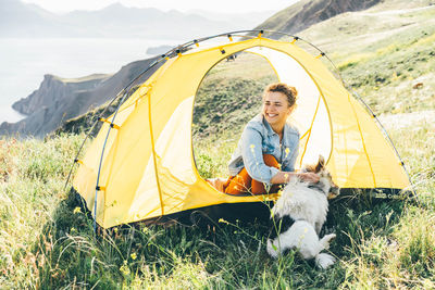 Woman resting with a dog on the seashore view from a tourist tent.