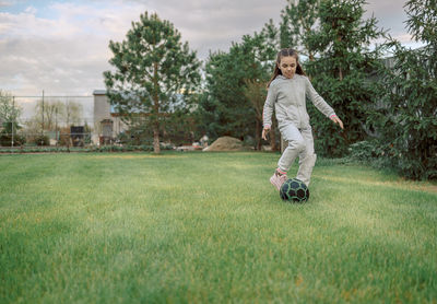 Cute little girl playing football with soccer ball on green lawn in backyard of house. child kicking 