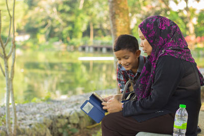 Mother and son using mobile phone while sitting in park