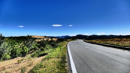 Scenic view of road by mountains against clear blue sky