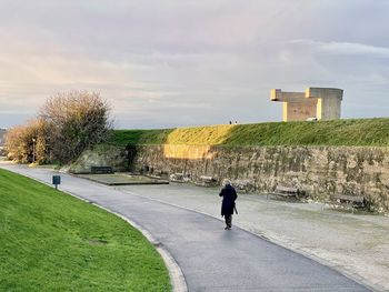 Rear view of man walking on footpath against sky