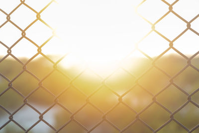 Close-up of chainlink fence against clear sky, metal mesh against the sun
