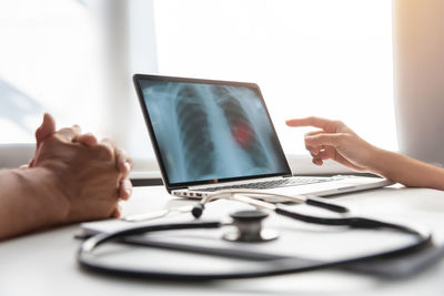 Cropped hands of patient by doctor pointing towards x-ray on laptop in clinic