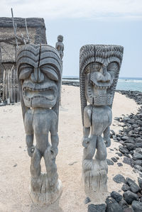 Statue on sand at beach against sky