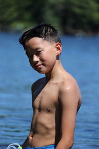 Portrait of shirtless boy standing by lake