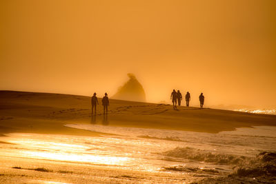 Silhouette people on beach against sky during sunset