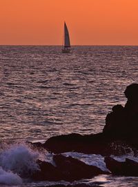 Silhouette sailboat in calm sea at sunset