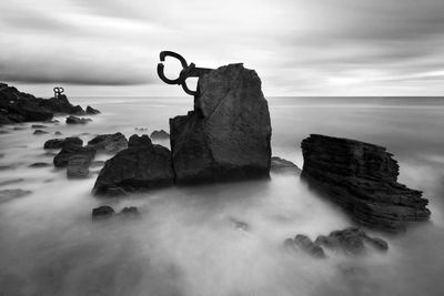 Rock formations in sea against cloudy sky