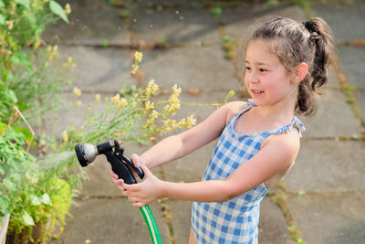 Young girl is watering plants in the backyard while wearing a bathing suit