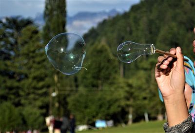 Cropped image of hand holding bubbles against trees