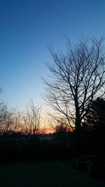 Silhouette bare trees on landscape against sky at sunset