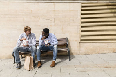 Multiracial friends talking and having food on bench