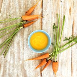 Top view of carrots and its pure in bowl kept on wooden surface