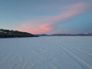 Snow covered land against sky during sunset