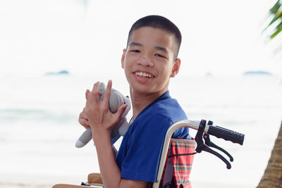 Portrait of boy sitting on wheelchair against sea