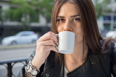 Close-up portrait of young woman drinking coffee at sidewalk cafe