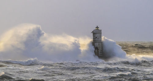 Lighthouse amidst sea and buildings against sky