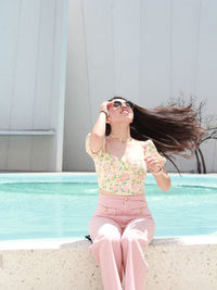 Portrait of young woman wearing sunglasses while sitting at beach