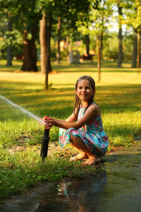 Happy six year old girl playing with a water sprinkler in the summer sunlit park