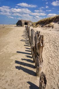 Wooden fence on sand against sky