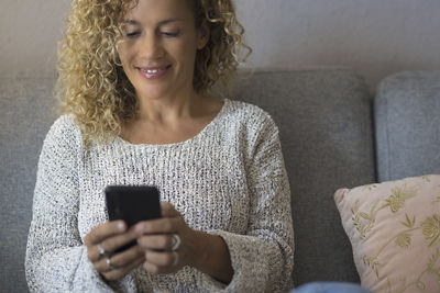 Portrait of young woman using phone while sitting on sofa at home