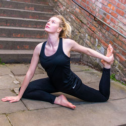 Young woman stretching on steps against brick wall