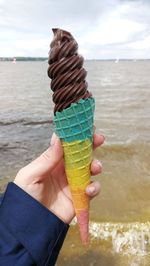 Hand holding ice cream cone on beach