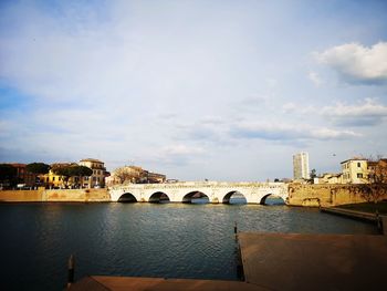 Bridge over river by buildings against sky