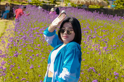 Beautiful young woman standing by purple flowering plants on field