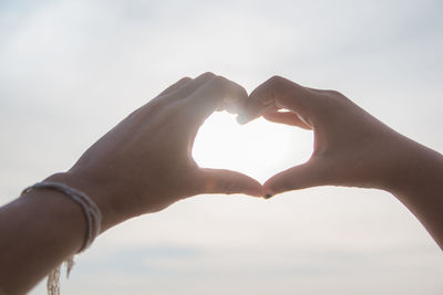 Midsection of woman making heart shape against sky