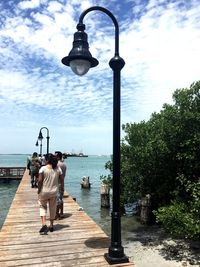 Rear view of people walking on jetty against sea