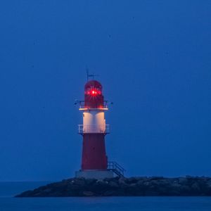 Lighthouse by sea against clear sky