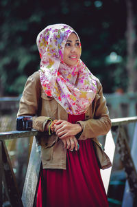 Portrait of young woman standing by railing