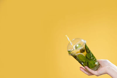 Midsection of person holding drink against yellow background