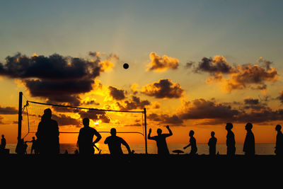Silhouette people playing volleyball at beach against sky during sunset