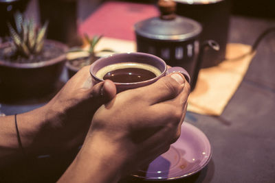 Close-up of hand holding coffee cup on table