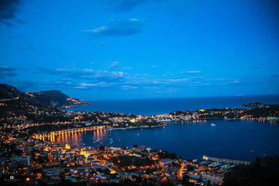 High angle view of illuminated city by sea against sky